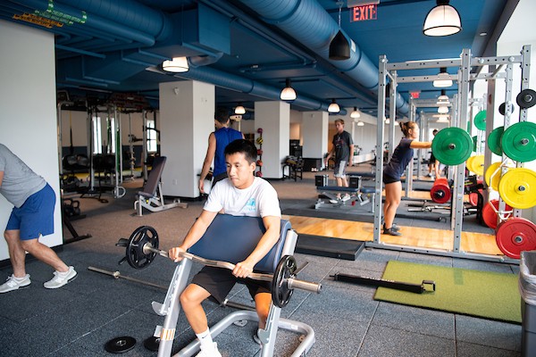 A student lifts weights as other student workout at the fitness center in the background.