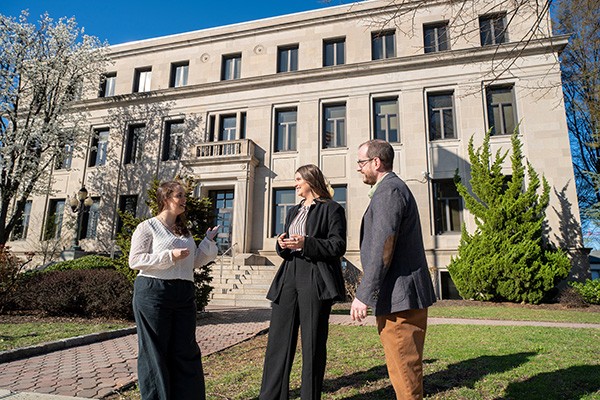 Two students and an alum from the Master in Public Administration program stand outside a township building.